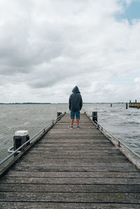 Rear view of teenager on jetty at sea against sky