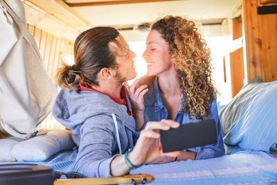 Smiling couple taking selfie while lying on bed in camping van