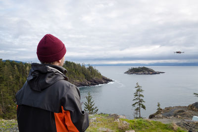 Rear view of man standing by sea against sky