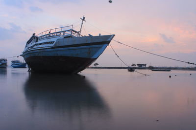 Fishing boat moored in sea against sky during sunset