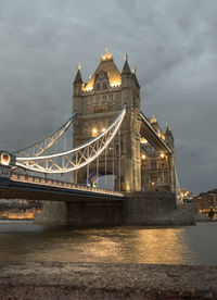 Illuminated bridge over river against sky at night