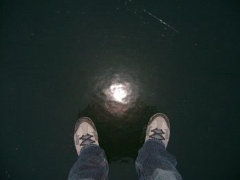 Low section of man standing on wet road at night