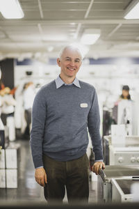 Portrait of smiling mature salesman standing in electronics store