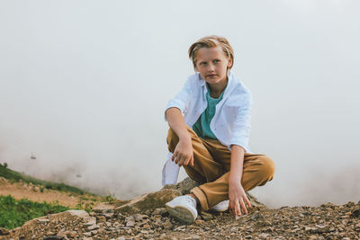 Portrait of smiling girl sitting on rock against sky