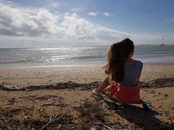 Young woman sitting on beach against sky