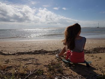 Young woman sitting at beach against sky