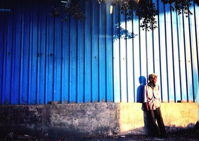 Man looking away while standing against blue wall