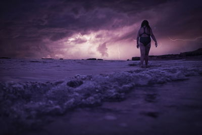 Woman standing on beach against sky during sunset