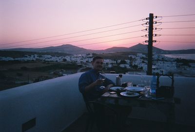 Man sitting at dusk against sky during sunset