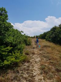 Woman on dirt road amidst trees against sky