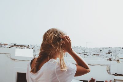 Close-up of young woman standing at building terrace against clear sky