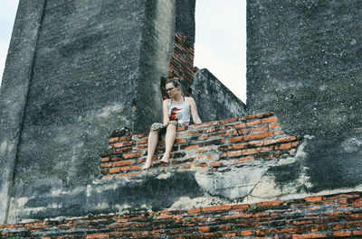 Low angle view of woman sitting on old brick wall