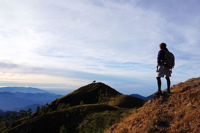 Rear view of man standing on mountain against sky