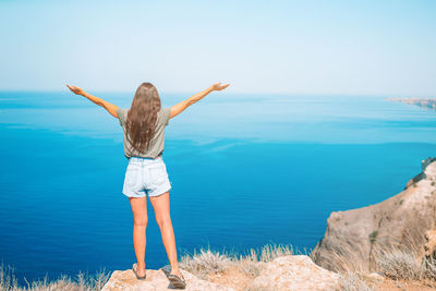 Rear view of woman standing by sea against sky