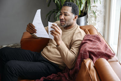 Mature man examining financial bills on sofa at home