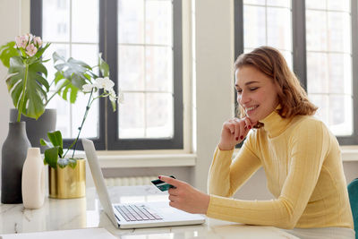 Young woman using phone while sitting on table at home