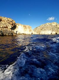 Rock formations on sea shore against blue sky