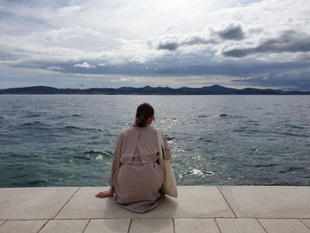 Rear view of woman sitting on sea against sky