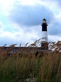 Lighthouse on field against cloudy sky