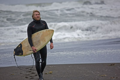 Young man walks with surfboard along beach in iceland