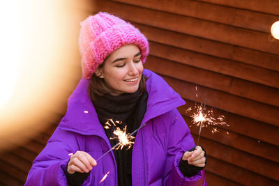 Happy young woman in outerwear with sparklers on the street on the background