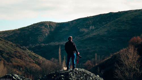 Man standing on rock looking at mountains against sky