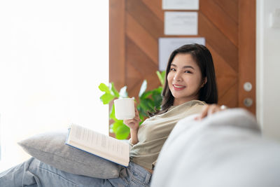 Portrait of young woman using mobile phone while sitting on bed at home