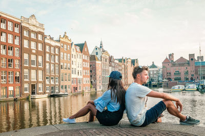 Woman sitting on canal against buildings in city