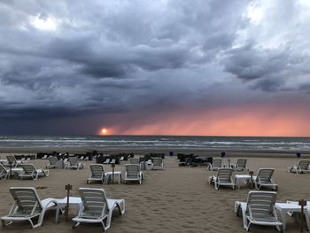 Chairs on beach against sky during sunset