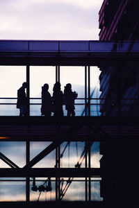 Silhouette people standing by railing against sky during sunset