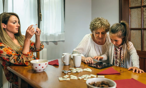 Woman photographing family playing mobile game at table