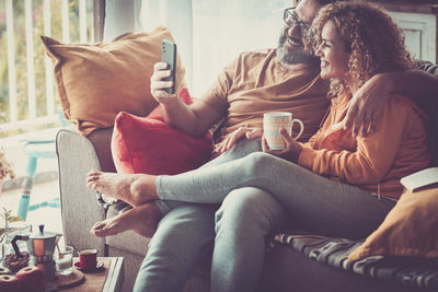 Smiling couple using smart phone while sitting at home