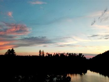 Reflection of silhouette trees in calm lake at sunset