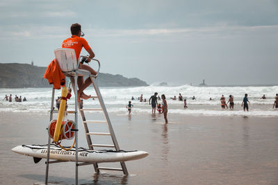 Rear view of people on beach against sky