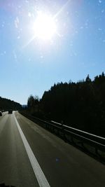 Road by trees against sky on sunny day