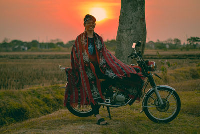 Portrait of smiling young man sitting on motorcycle at farm during sunset