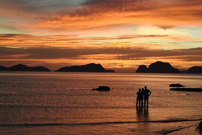 Silhouette people on beach against sky during sunset