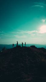 People standing on rock by sea against sky during sunset