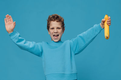 Portrait of young woman with arms raised standing against blue background