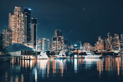 Illuminated buildings by river against sky at night in panama
