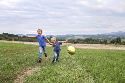 Boy playing with ball on field against sky