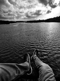 Low section of man relaxing by lake against sky