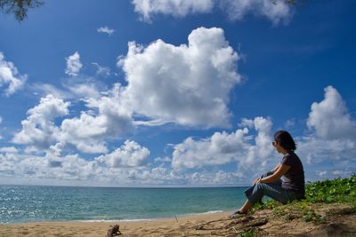 Woman sitting on beach against sky