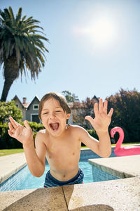 Full length of happy boy with swimming pool against sky