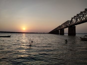 Silhouette bridge over sea against sky during sunset