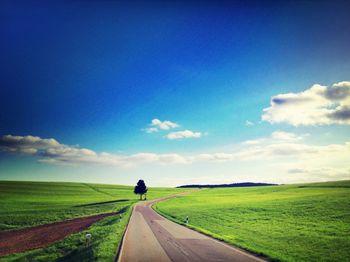 Country road on grassy field against cloudy sky