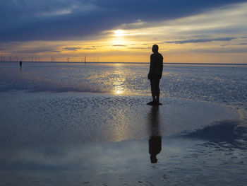 Silhouette woman standing on beach against sky during sunset