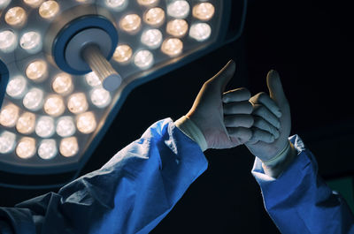 Cropped hands of surgeon giving fist bumps against illuminated lighting equipment