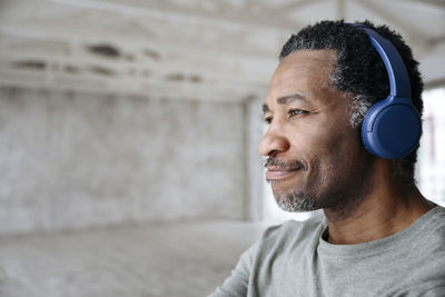 Smiling man listening to music through wireless headphones at home