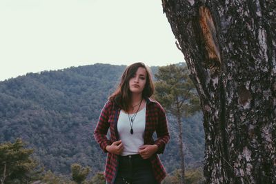 Young woman standing by tree against sky